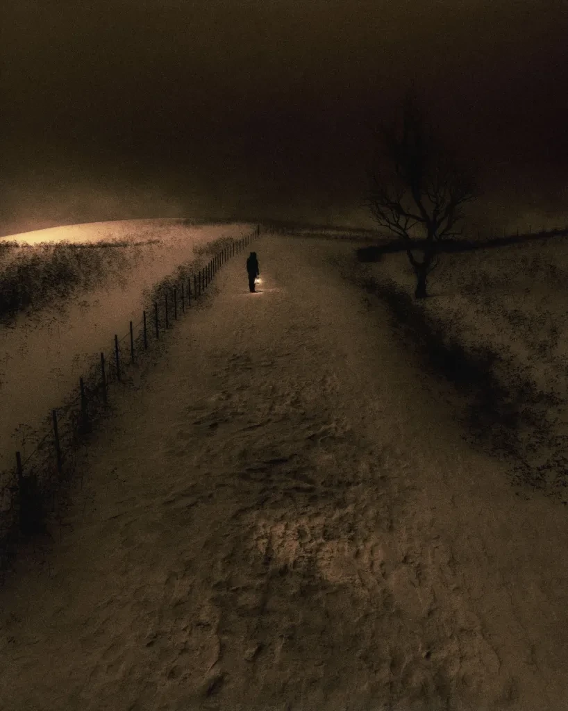 A lone figure with a lantern on a snowy path at night